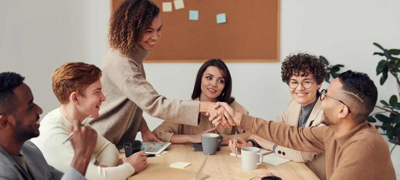 Business professionals shaking hands across a table during a collaborative advisory meeting.